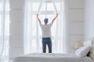 young man opening curtains in the morning 